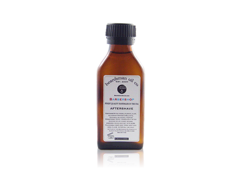 A small amber glass bottle of Beardsman Oil Co. after shave with a black ribbed cap and a white label, centered on a white background with a faint reflection below.