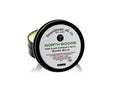 A tin of North Woods Beard Balm by Beardsman Oil Co, featuring a black metal container with a white lid label, shown on a white background with a reflection.