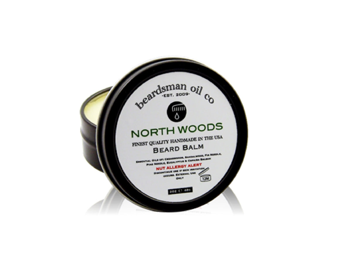 A tin of North Woods Beard Balm by Beardsman Oil Co, featuring a black metal container with a white lid label, shown on a white background with a reflection.